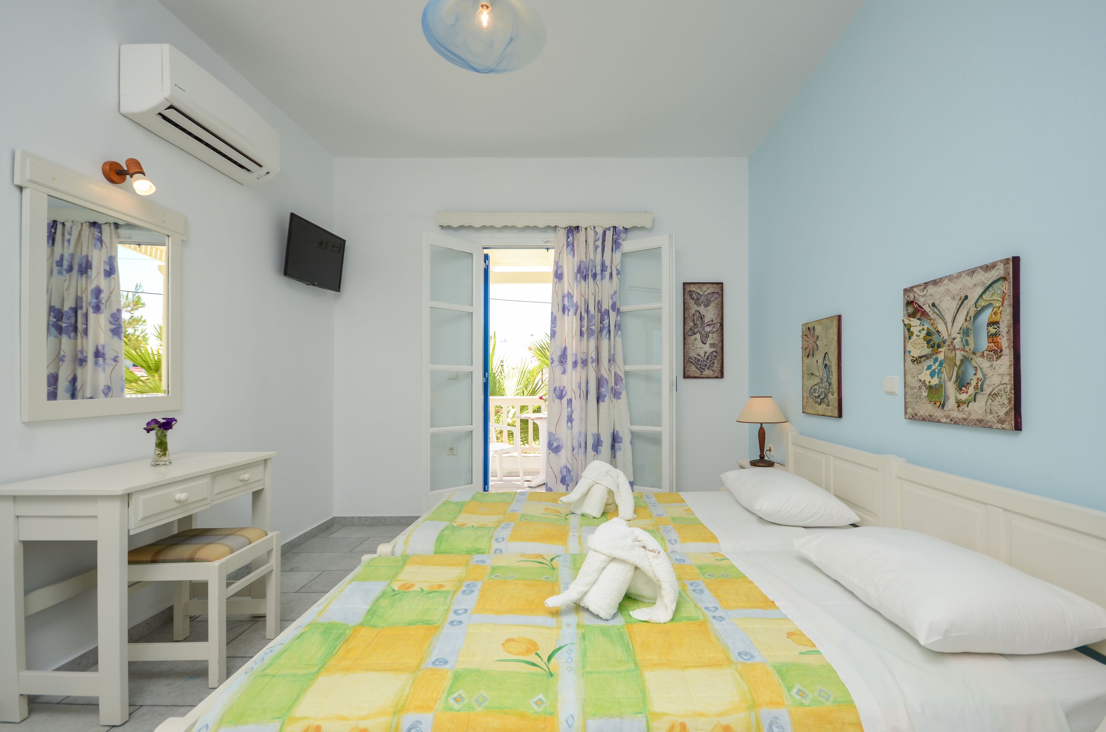 A hotel room with a bed, a desk, a chair, a TV, and a balcony with curtains.