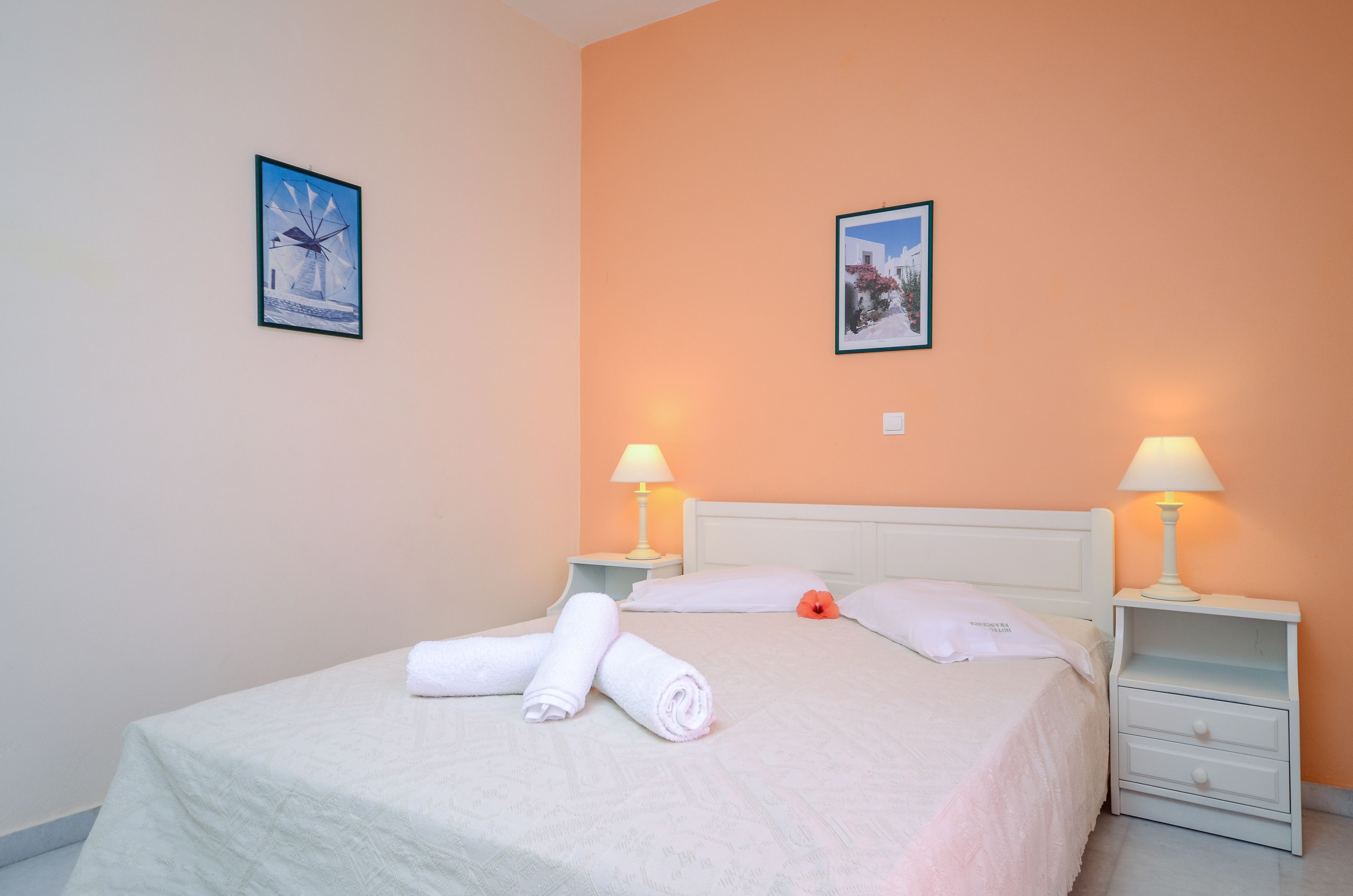 Un lit bien fait, agrément é de serviettes blanches pliées en rouleau, deux tables de chevet avec des lampes et deux tableaux encadrés accrochés aux murs.