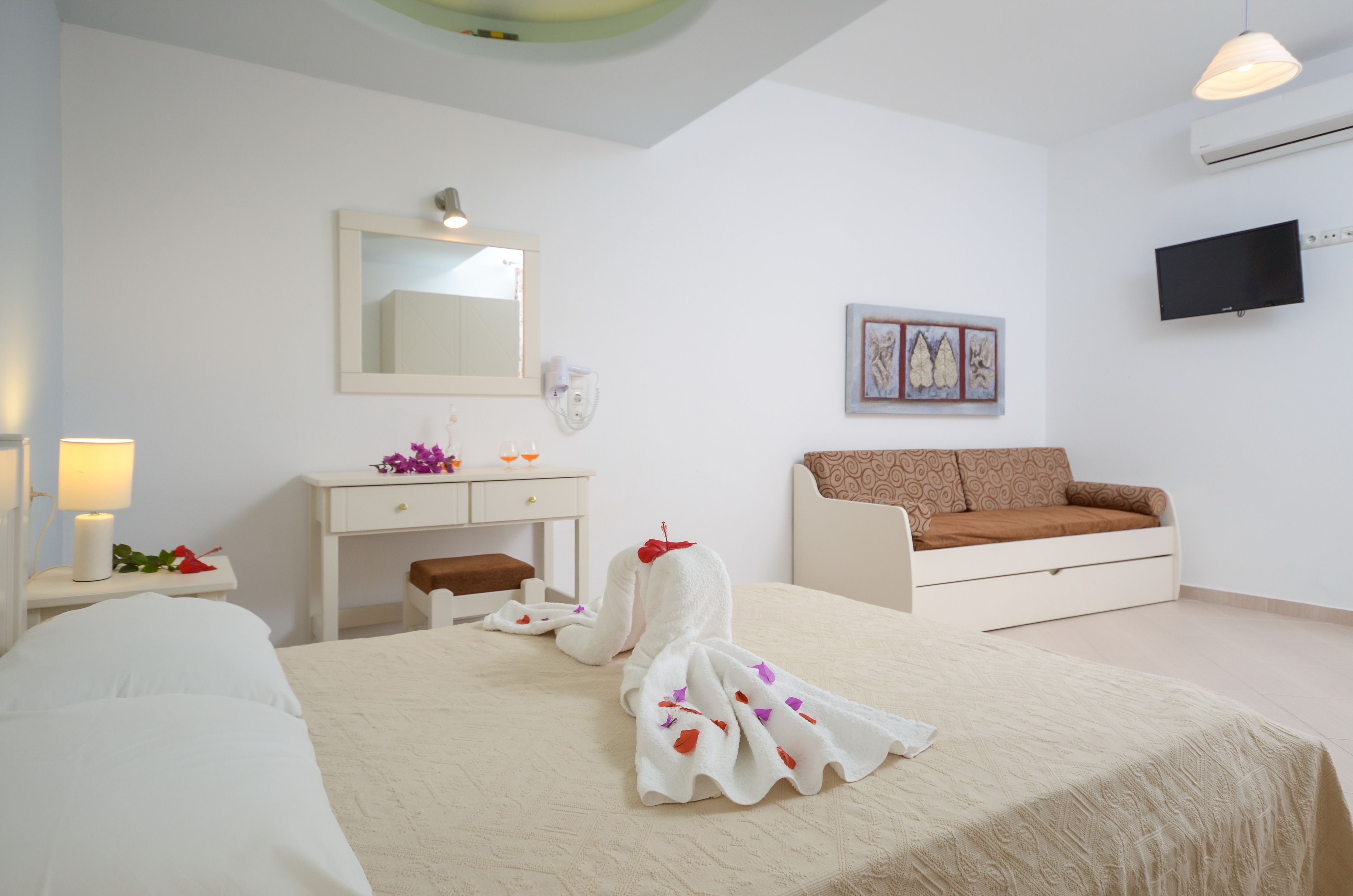 Una camera d'albergo con un letto, un comodino con una lampada, una piccola scrivania, un divano e una TV a parete.