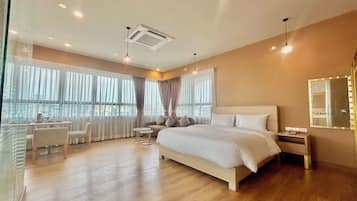 Una habitación de hotel moderna con una cama grande, un escritorio y una silla. Hay ventanas amplias con cortinas, un ventilador de techo y un espejo en la pared.