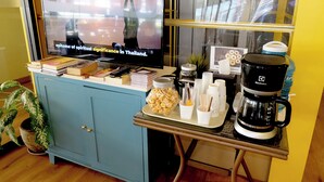 A hotel reception area with a television displaying a news program, a coffee machine, a tray with snacks, and a blue cabinet. - Siri Oriental Bangkok Hotel (Bangkok)