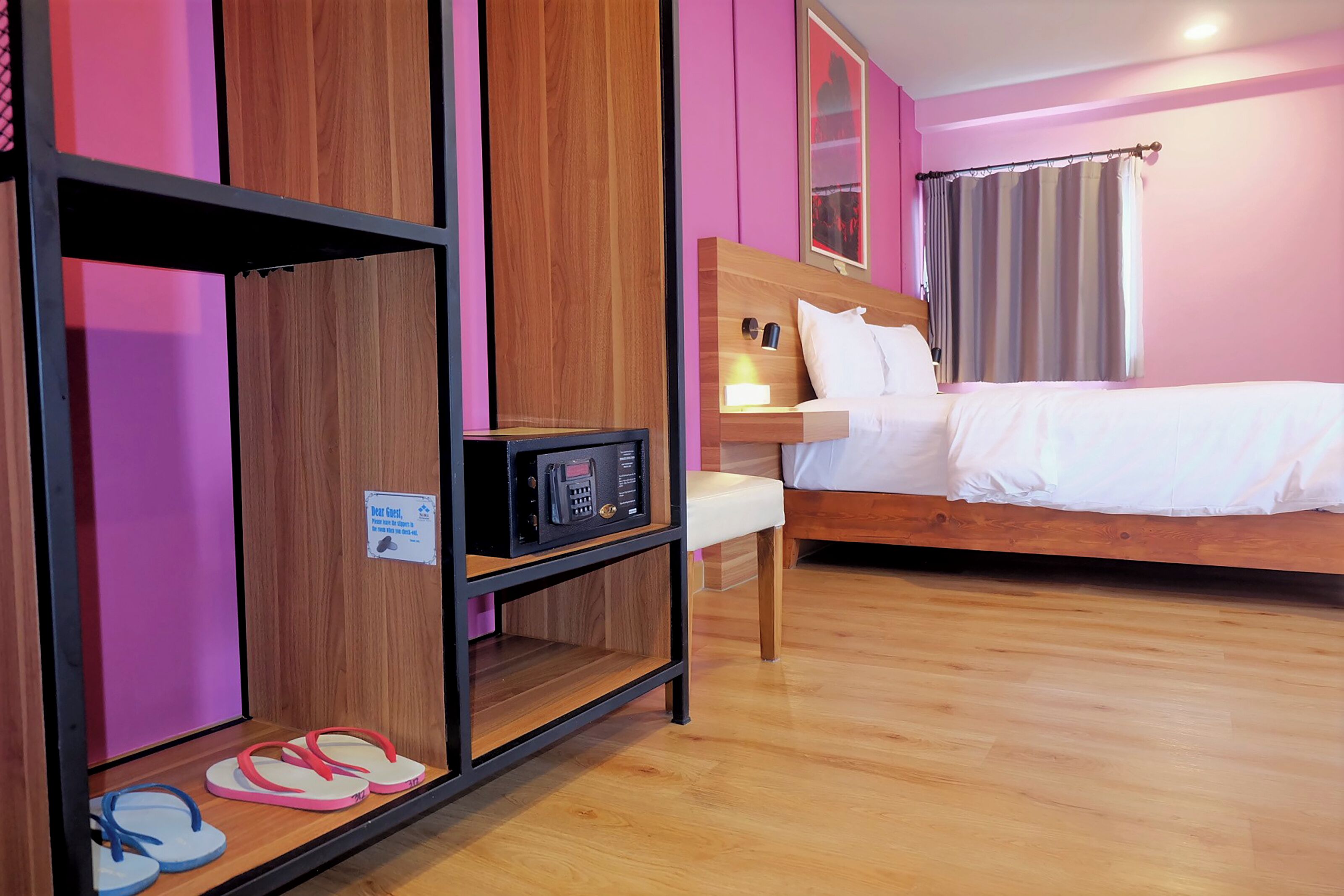 A hotel room with a wooden bed, a bedside table with a lamp, a shelf with flip-flops, and a sign indicating a guest room.