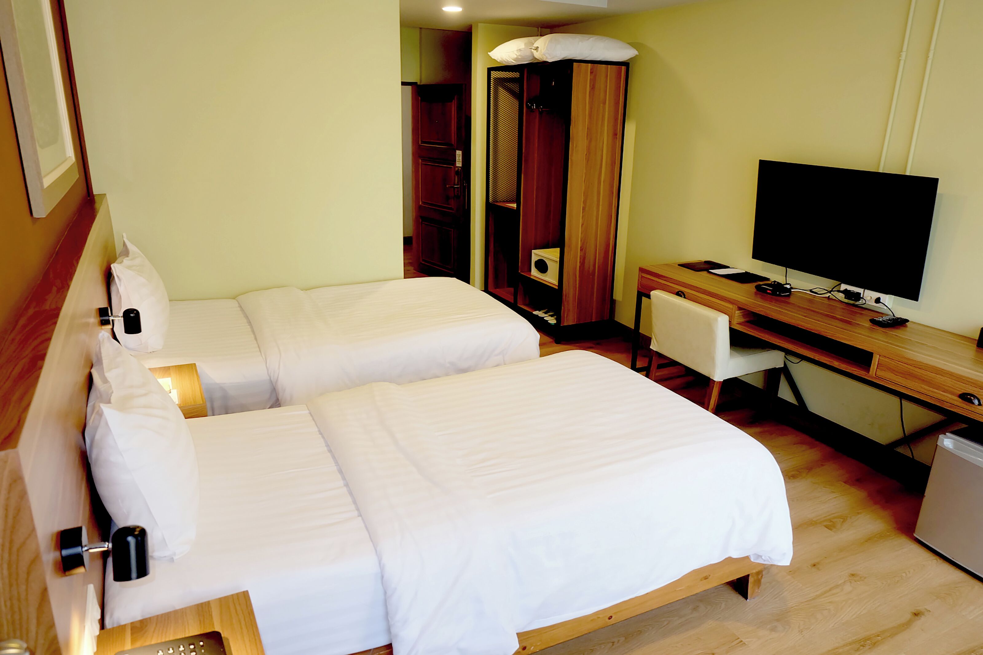 A hotel room with two beds, a desk with a television, and a wardrobe.