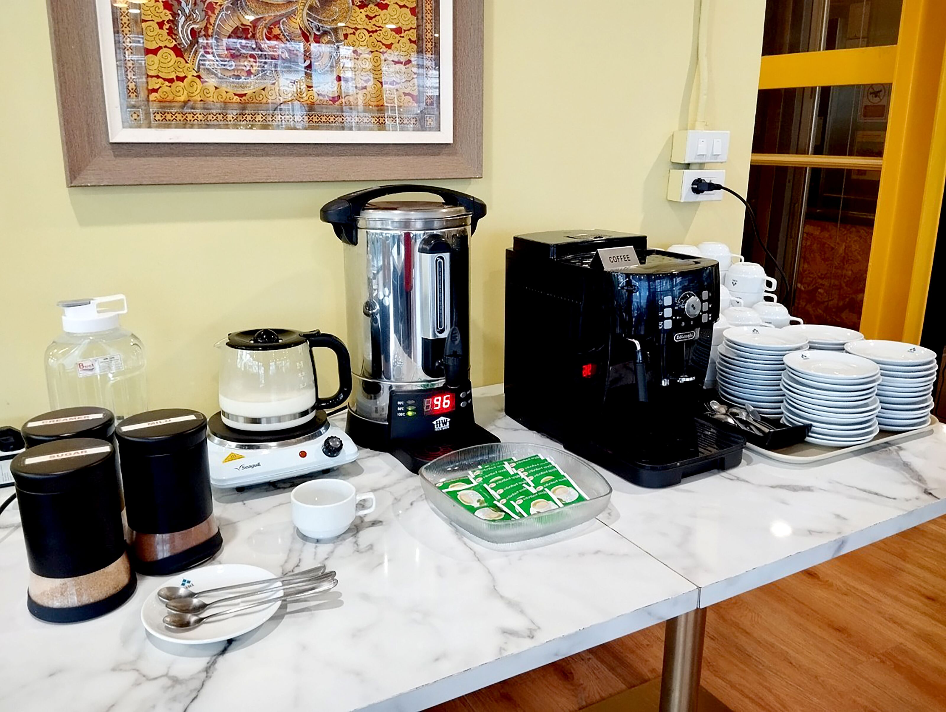 Un coin petit-déjeuner avec des machines à café, des sucriers, un pot à lait et une machine à café, le tout disposé sur un comptoir en marbre.