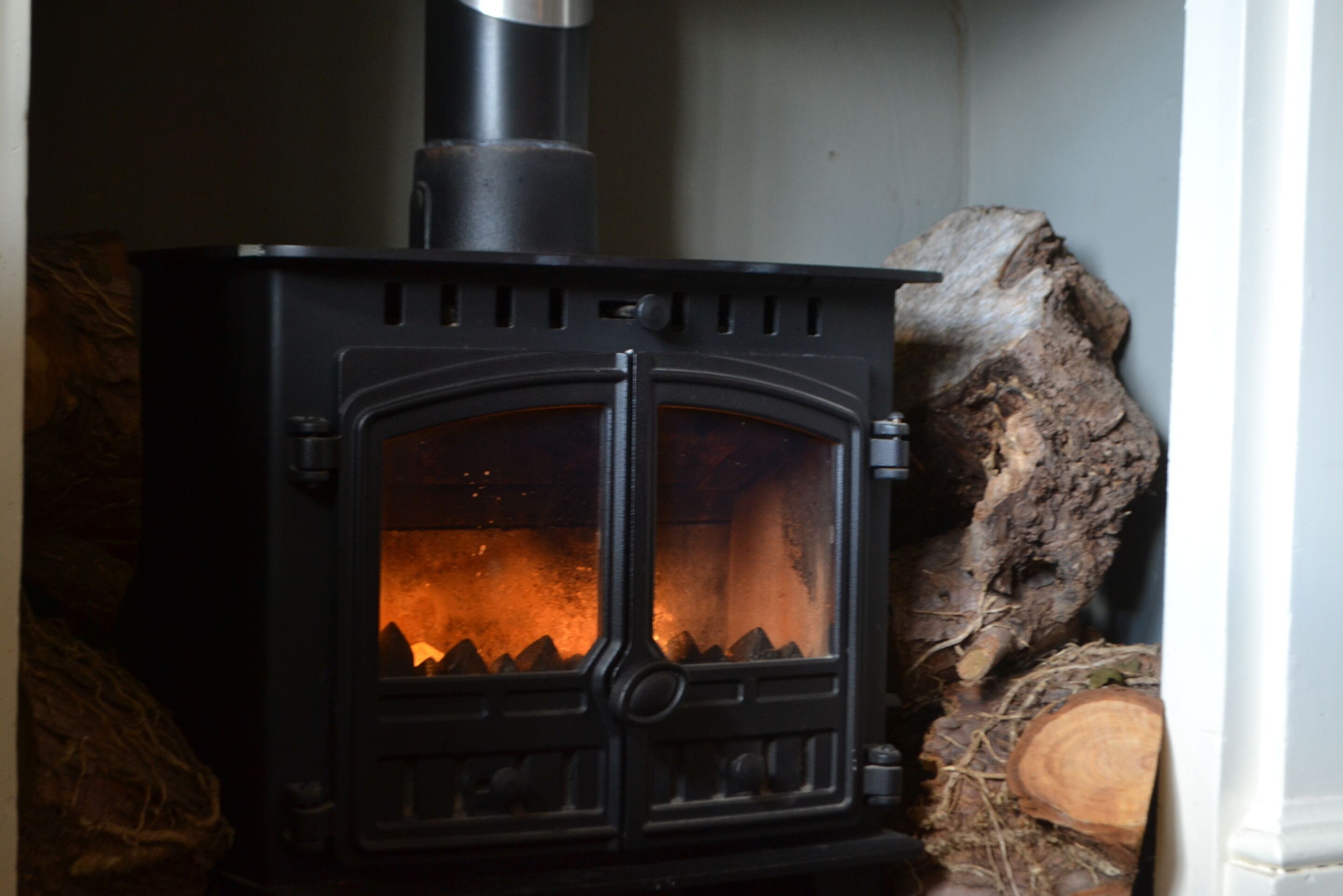 A wood-burning stove with a glass door, logs stacked beside it, and a rustic interior.