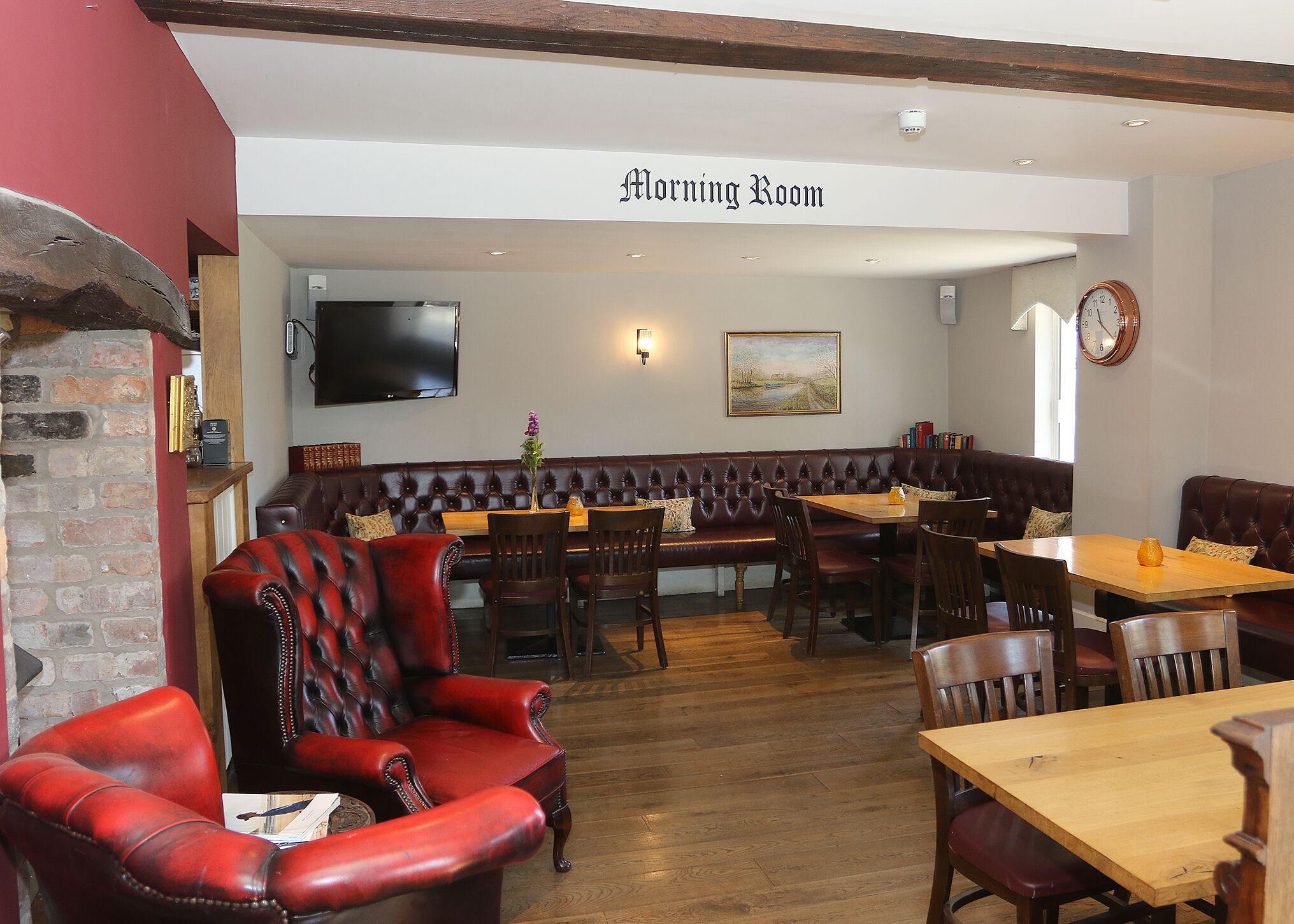 Een restaurant met een bord waarop 'Morning Room' staat, lederen zitplaatsen, houten tafels en een flatscreen aan de muur.