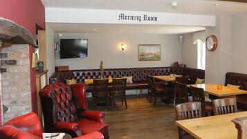 Een restaurant met een bord waarop 'Morning Room' staat, lederen zitplaatsen, houten tafels en een flatscreen aan de muur.