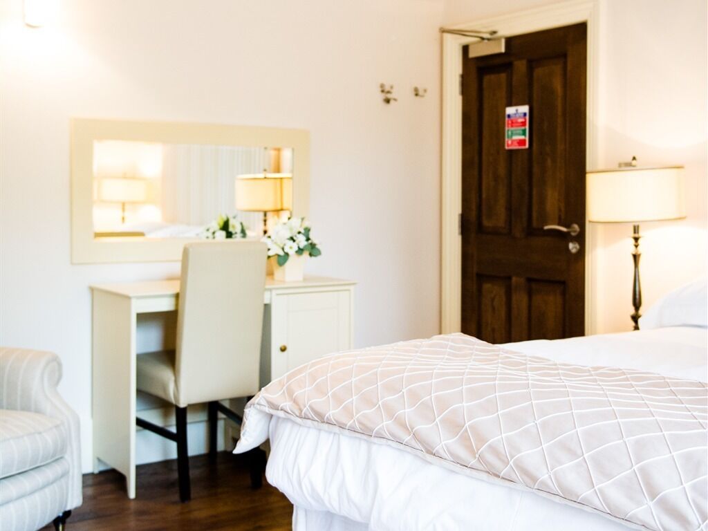 Una camera d'albergo con un letto, una scrivania, una sedia, un comò e una porta.