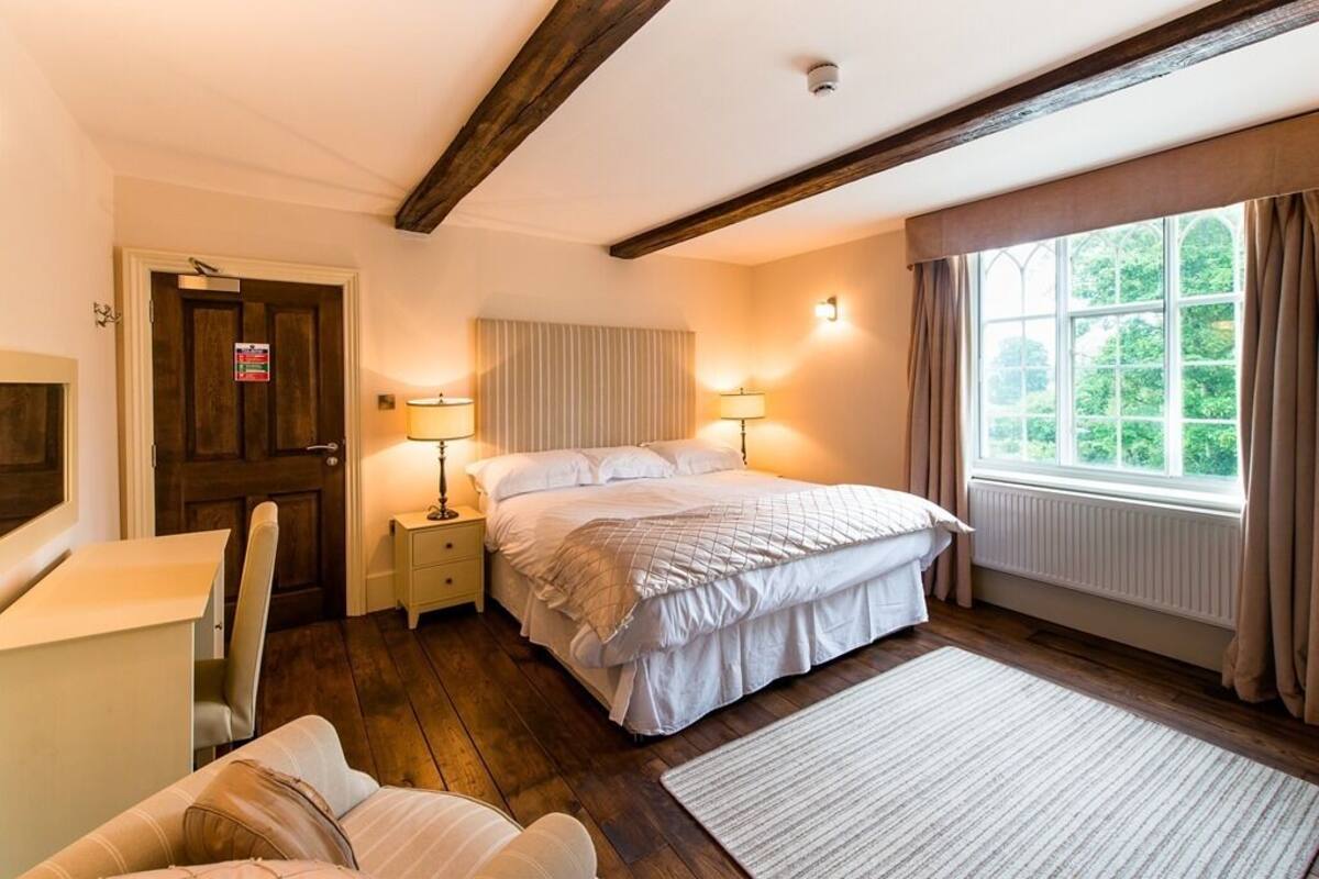 Une chambre à coucher avec un lit, des tables de chevet, un bureau et une fenêtre avec des rideaux.