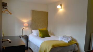 Habitación de hotel con cama, mesita de noche, lámpara y perchero.