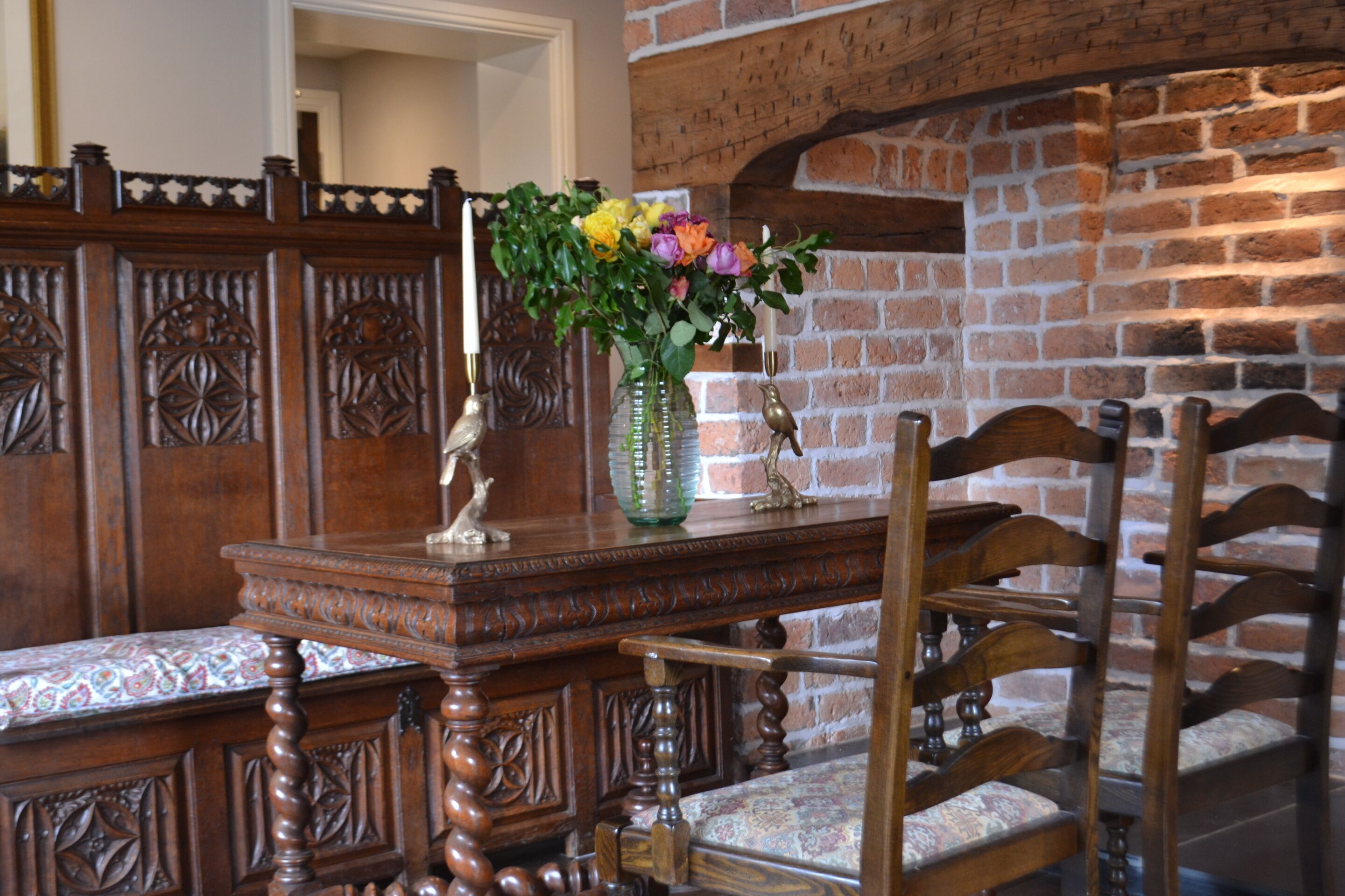 A wooden dining table with a vase of flowers, a candle, and a bird statue.
