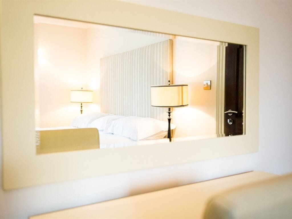 A hotel room with a bed, bedside lamps, a mirror, and a door.
