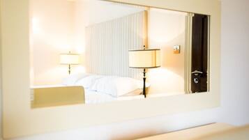 A hotel room with a bed, bedside lamps, a mirror, and a door.