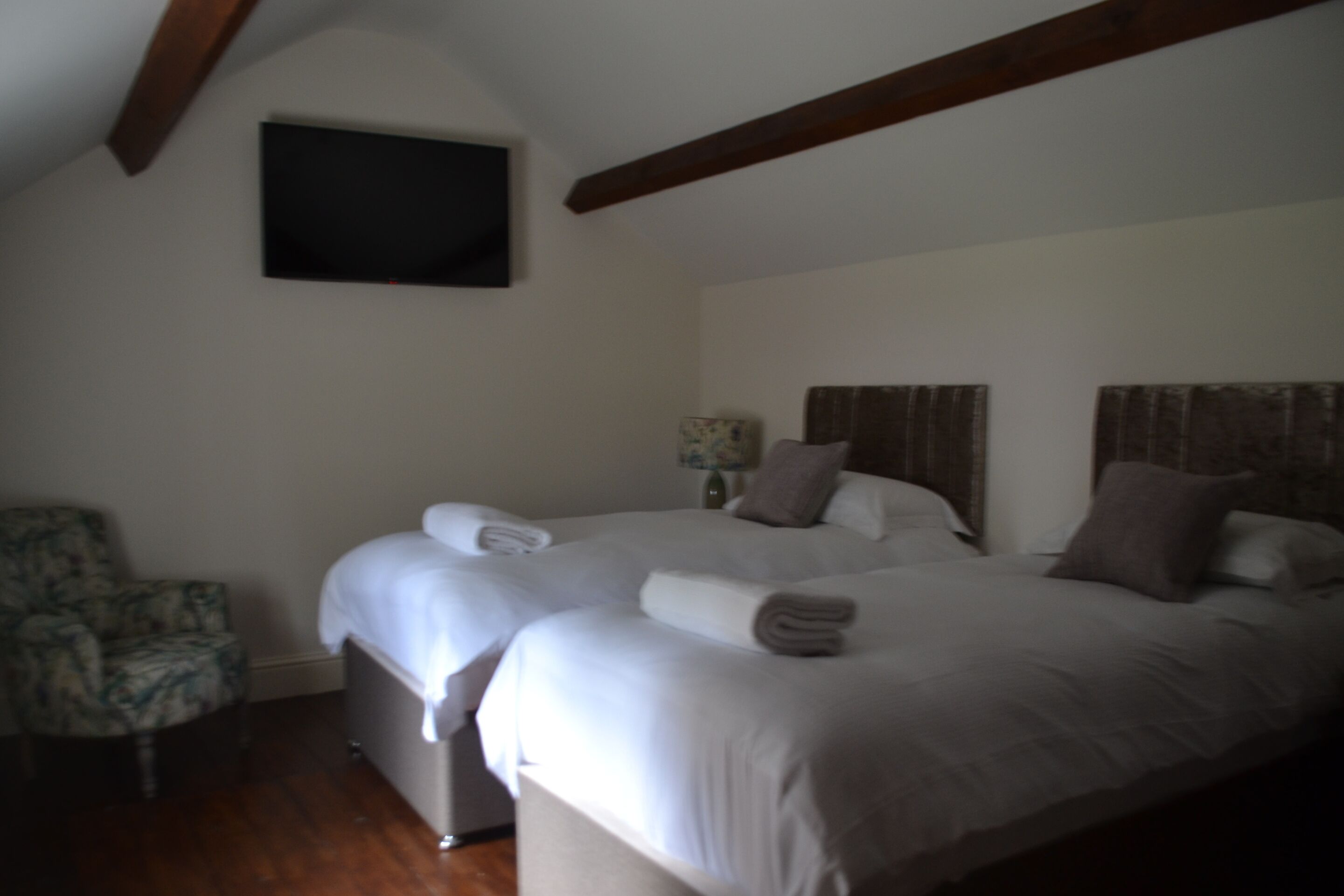 A bedroom with two beds, a chair, and a television mounted on the wall.