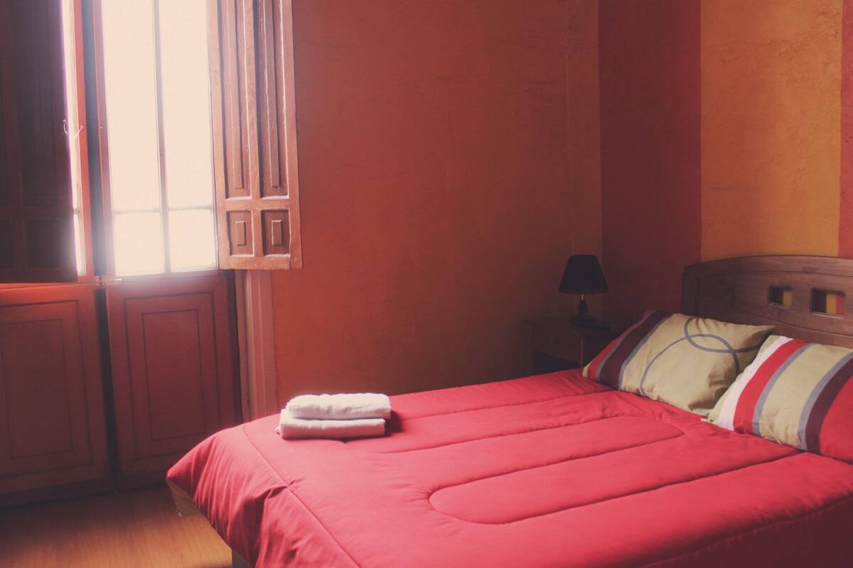 A bedroom with a bed, a nightstand, a lamp, and a window with curtains.