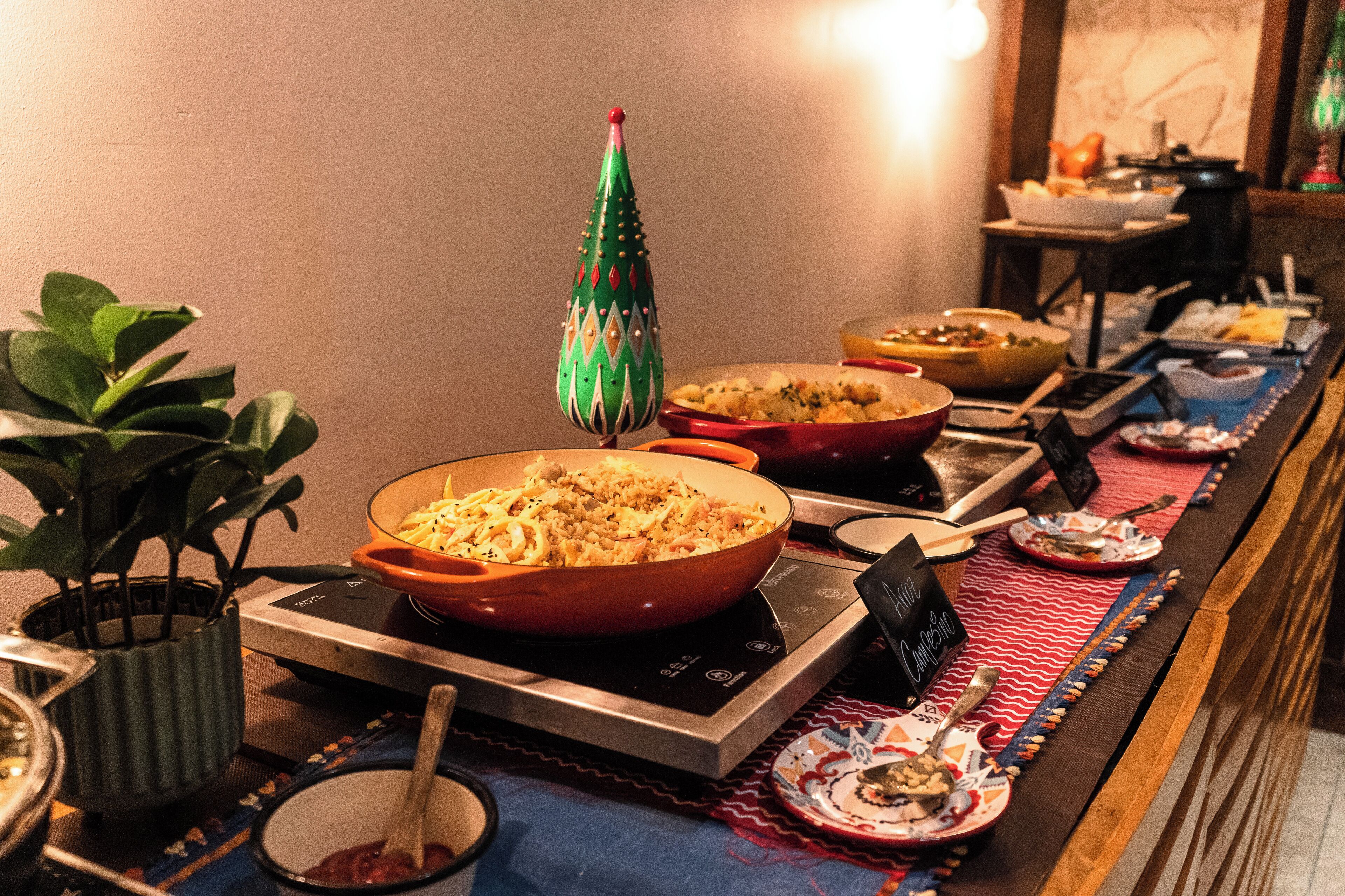 Una mesa de buffet con diversos platos, un árbol decorativo navideño y una planta en maceta.