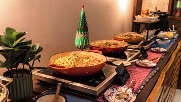 Una mesa de buffet con diversos platos, un árbol decorativo navideño y una planta en maceta.