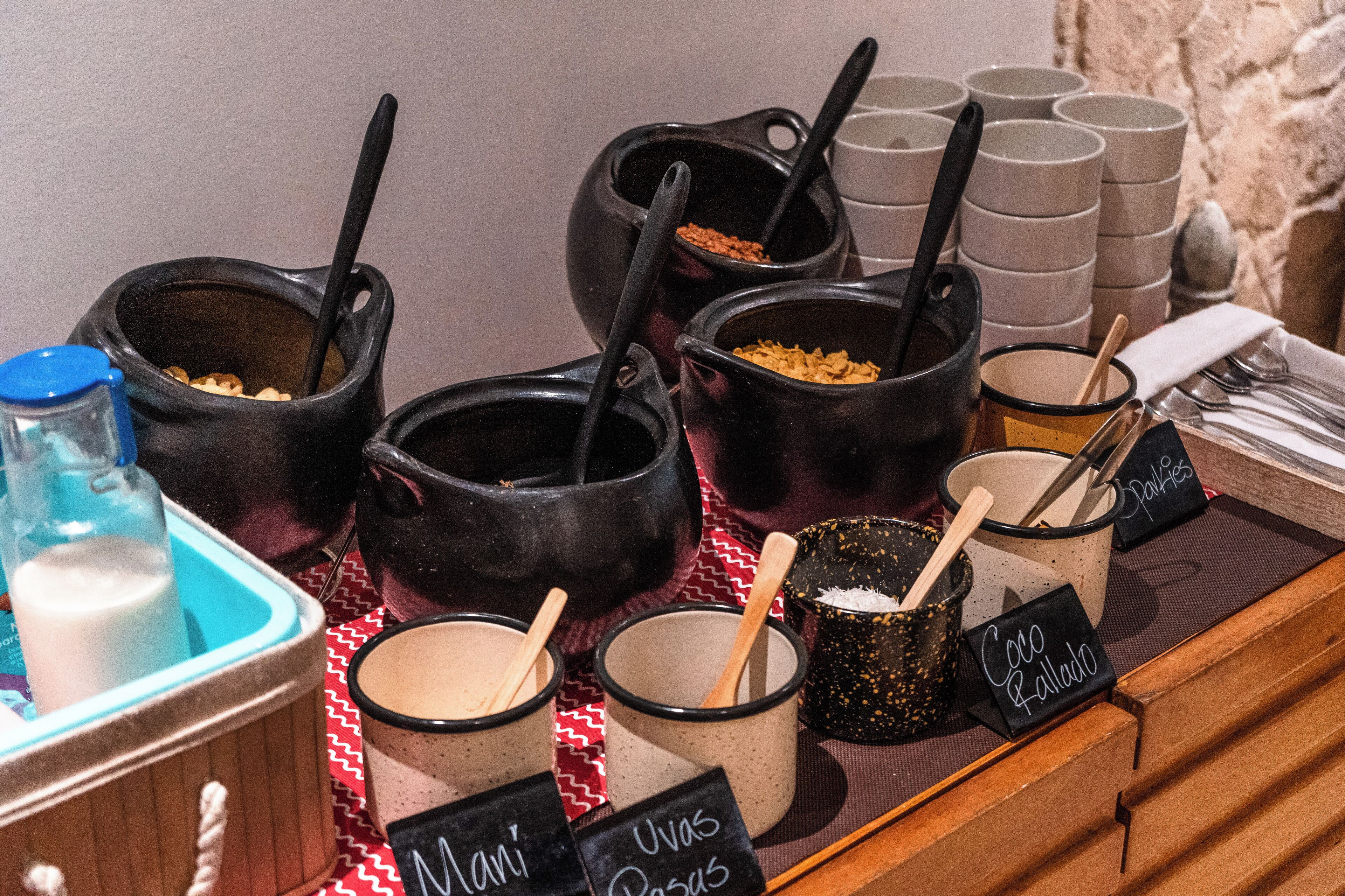 A buffet setup with various food items in black and white pots, labeled with names like "Coco Rellado" and "Uvas Pasas".