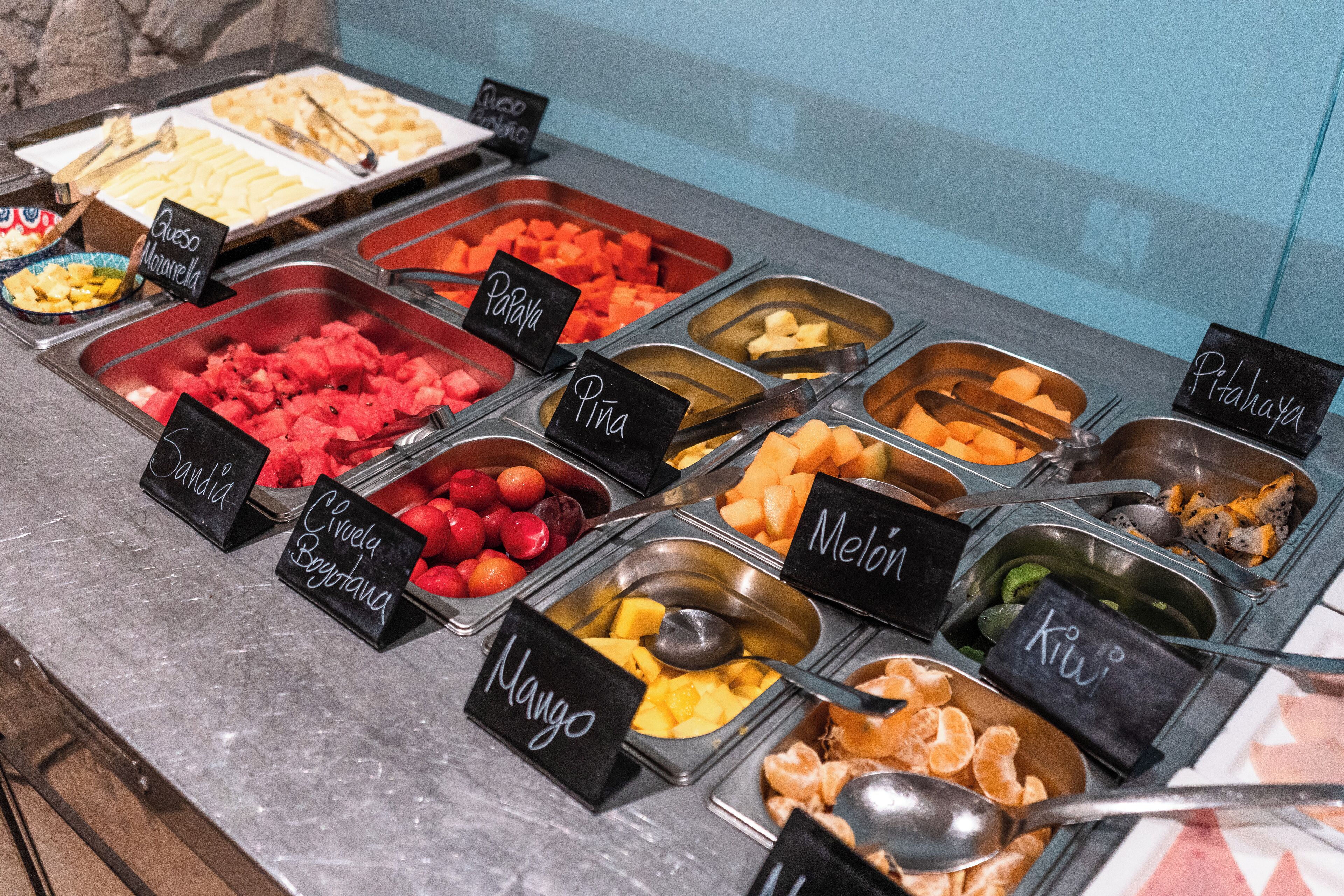 Un bufé con diversas frutas y quesos, incluyendo mango, papaya y granada.