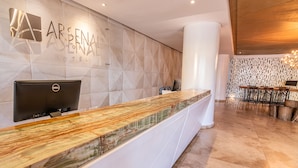 L’hôtel Arsenal dispose d’un comptoir d’accueil au design moderne, avec un comptoir en marbre et un grand logo sur le mur.