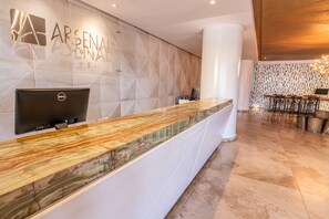 L’hôtel Arsenal dispose d’un comptoir d’accueil au design moderne, avec un comptoir en marbre et un grand logo sur le mur.