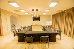 Ein Konferenzraum mit langem Tisch, Stühlen, einer Chandelierleuchtre, einer Whiteboard-Tafel und Vorhängen.