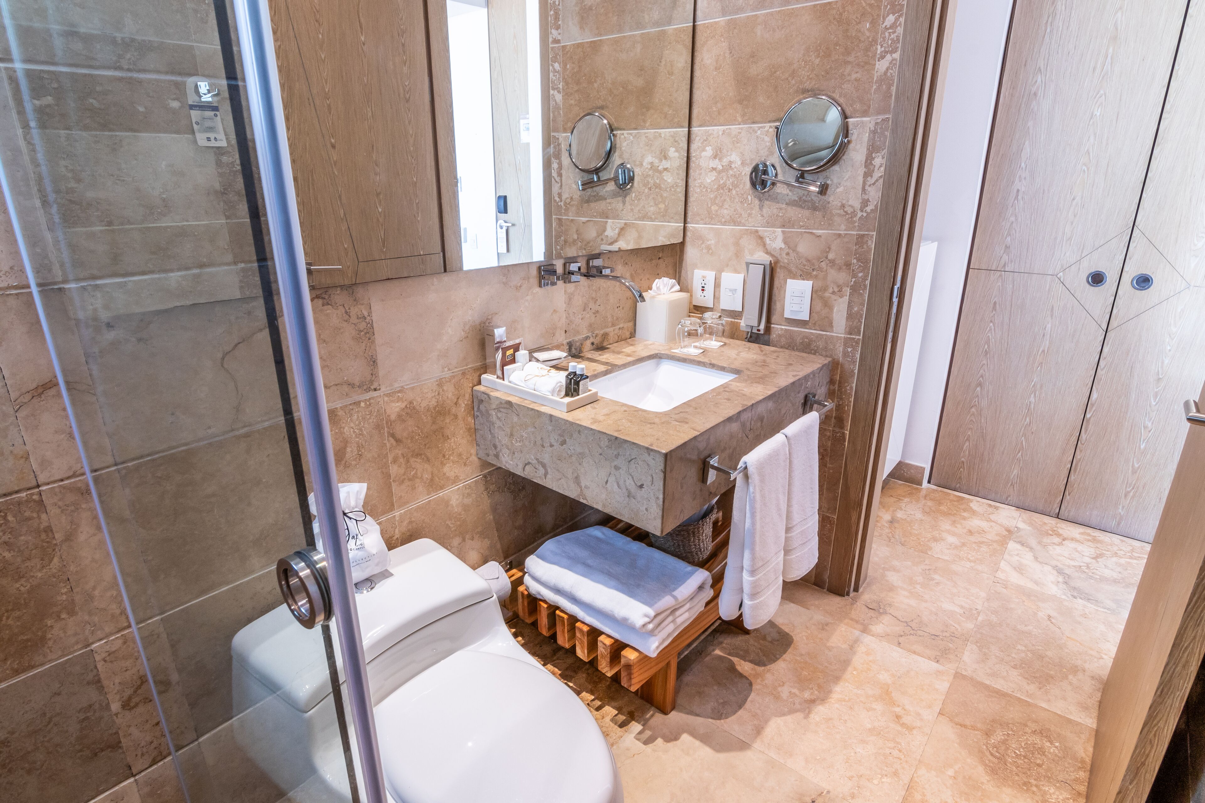 Une salle de bain moderne avec une douche à parois de verre, un lavabo en marbre et des toilettes dotées d’un meuble-lavabo en bois.