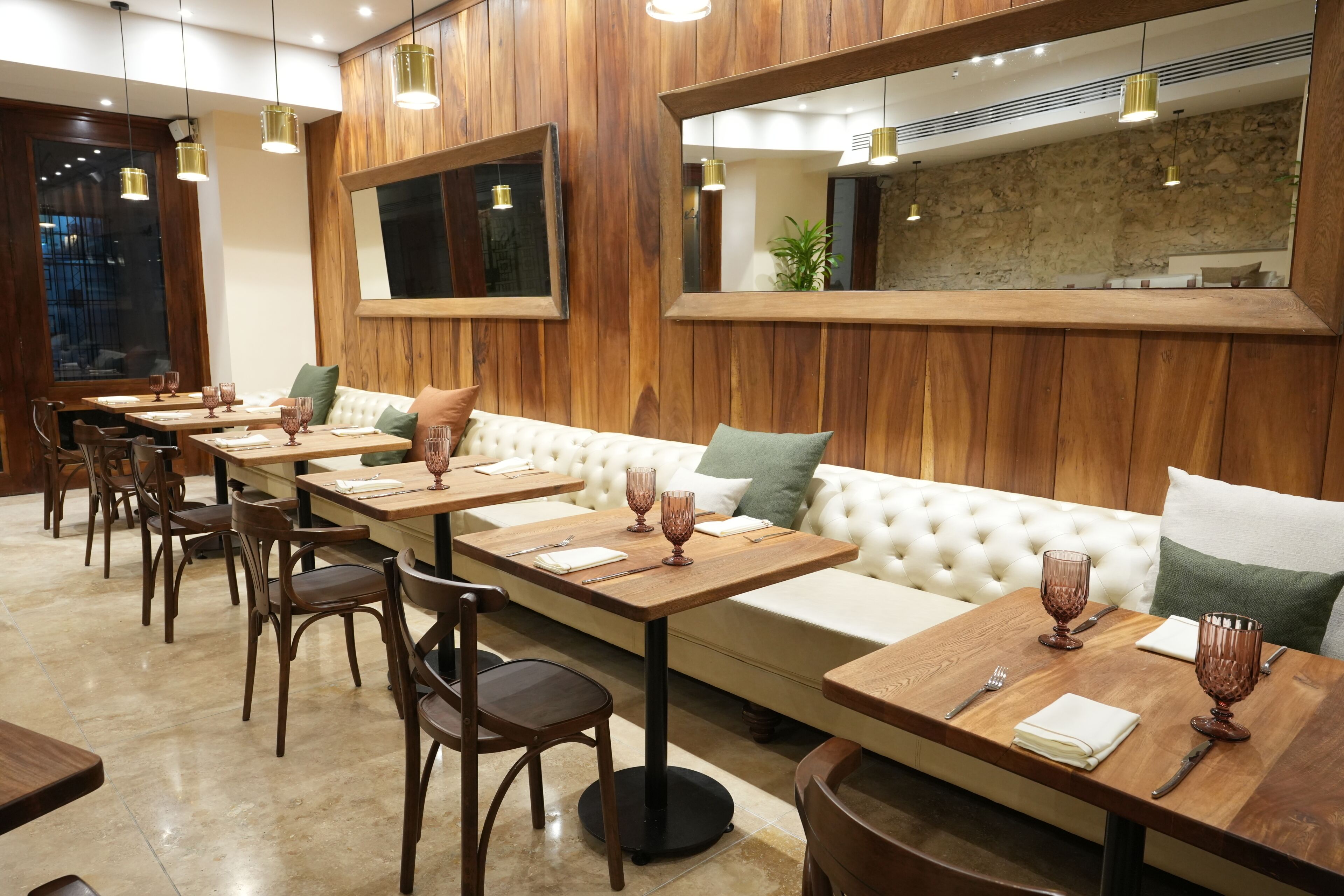 A restaurant interior with wooden paneling, a long dining table, cushioned seating, and pendant lighting.