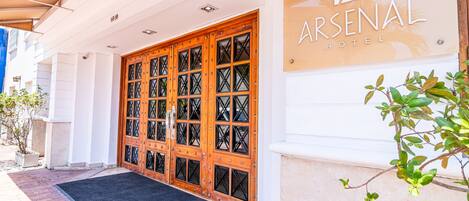 L'ingresso di un hotel con un'ampia porta in legno, un tappetino nero e un cartello che riporta la scritta 'ARSENAL HOTEL'.