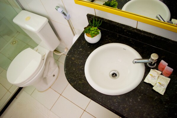 Un baño con inodoro, lavabo y una pequeña planta en maceta sobre el mostrador.