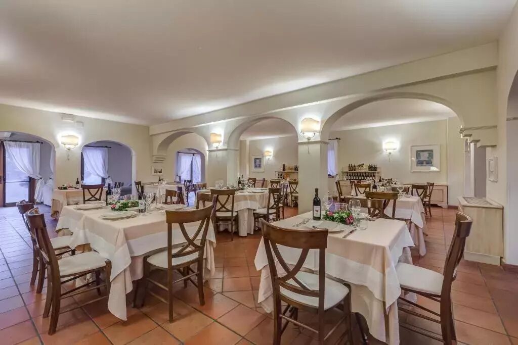A dining area with multiple tables set for meals, featuring white tablecloths and wooden chairs.