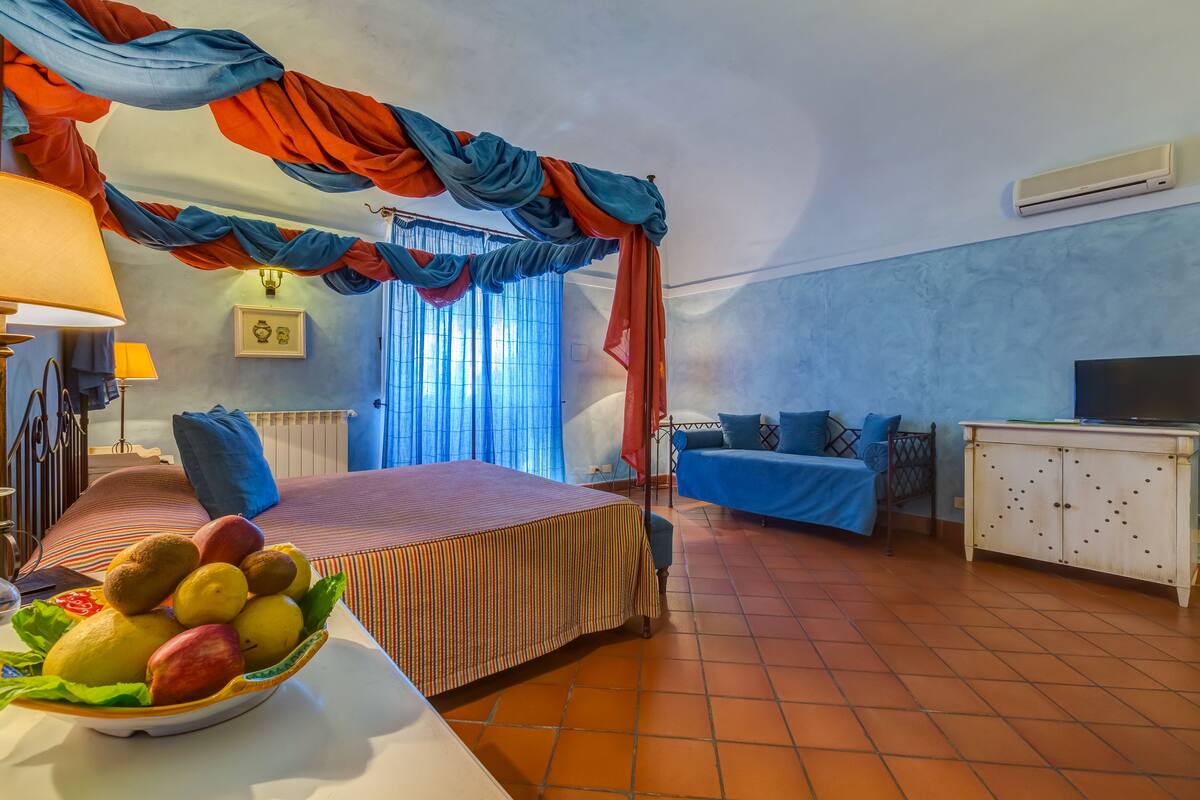 Une pièce comprenant un lit, une télévision, un canapé, une armoire et un panier de fruits.