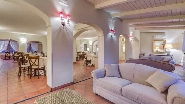 Un vaste espace de vie comprenant un canapé, une table à manger et des chaises. On aperçoit des arcades et une cuisine au fond.