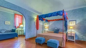 Une chambre à coucher avec un lit à baldaquin, deux poufs bleus, une table de chevet et un canapé.