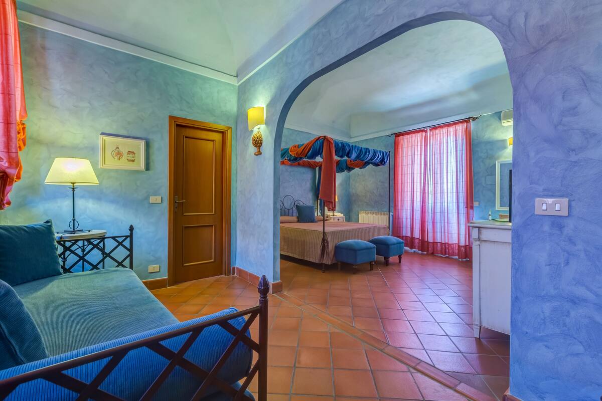 Une chambre à coucher avec un lit, une table de chevet, une lampe et une fenêtre avec des rideaux.