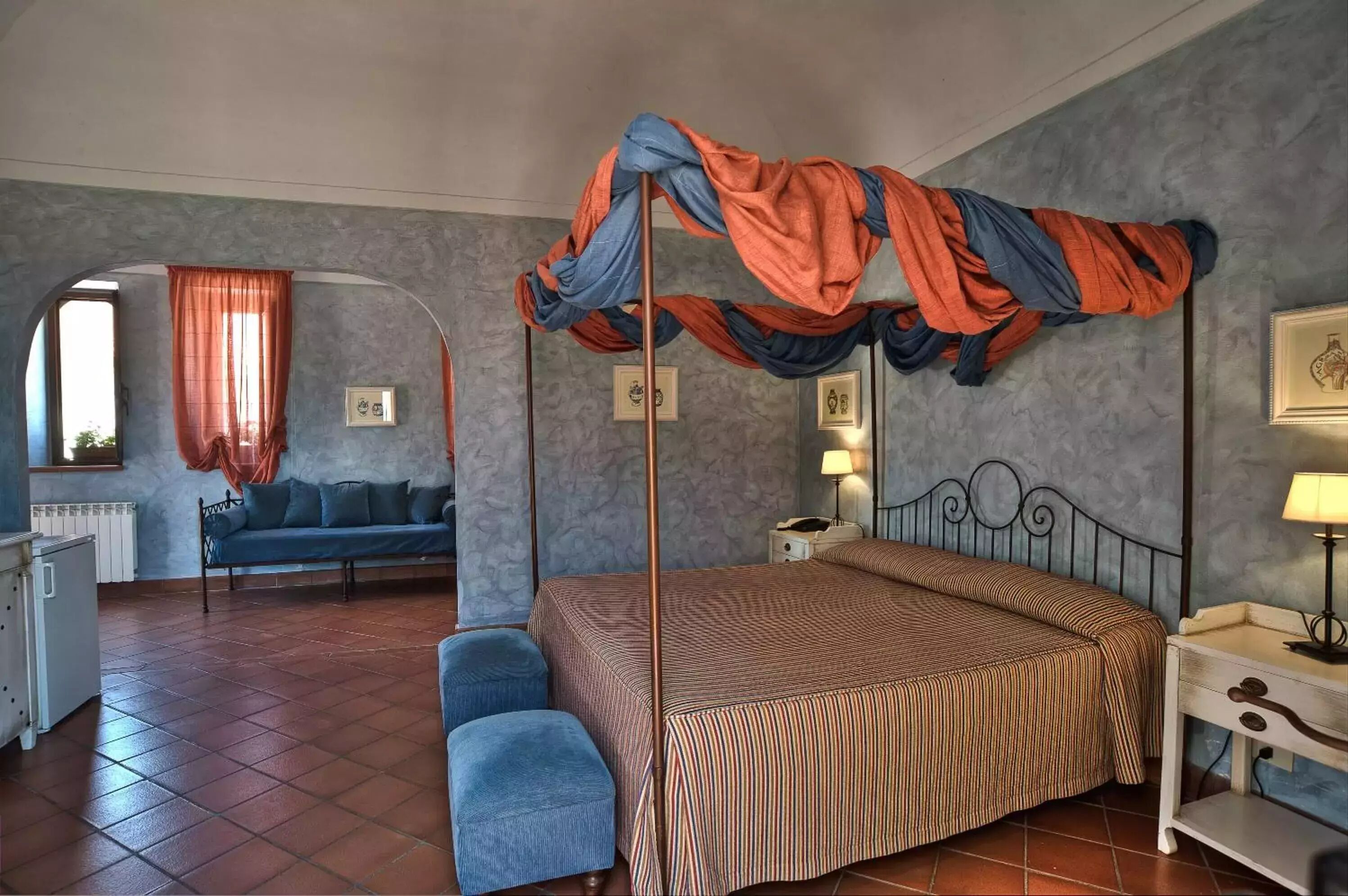 A bedroom with a four-poster bed, a sofa, a small table, and a chair.