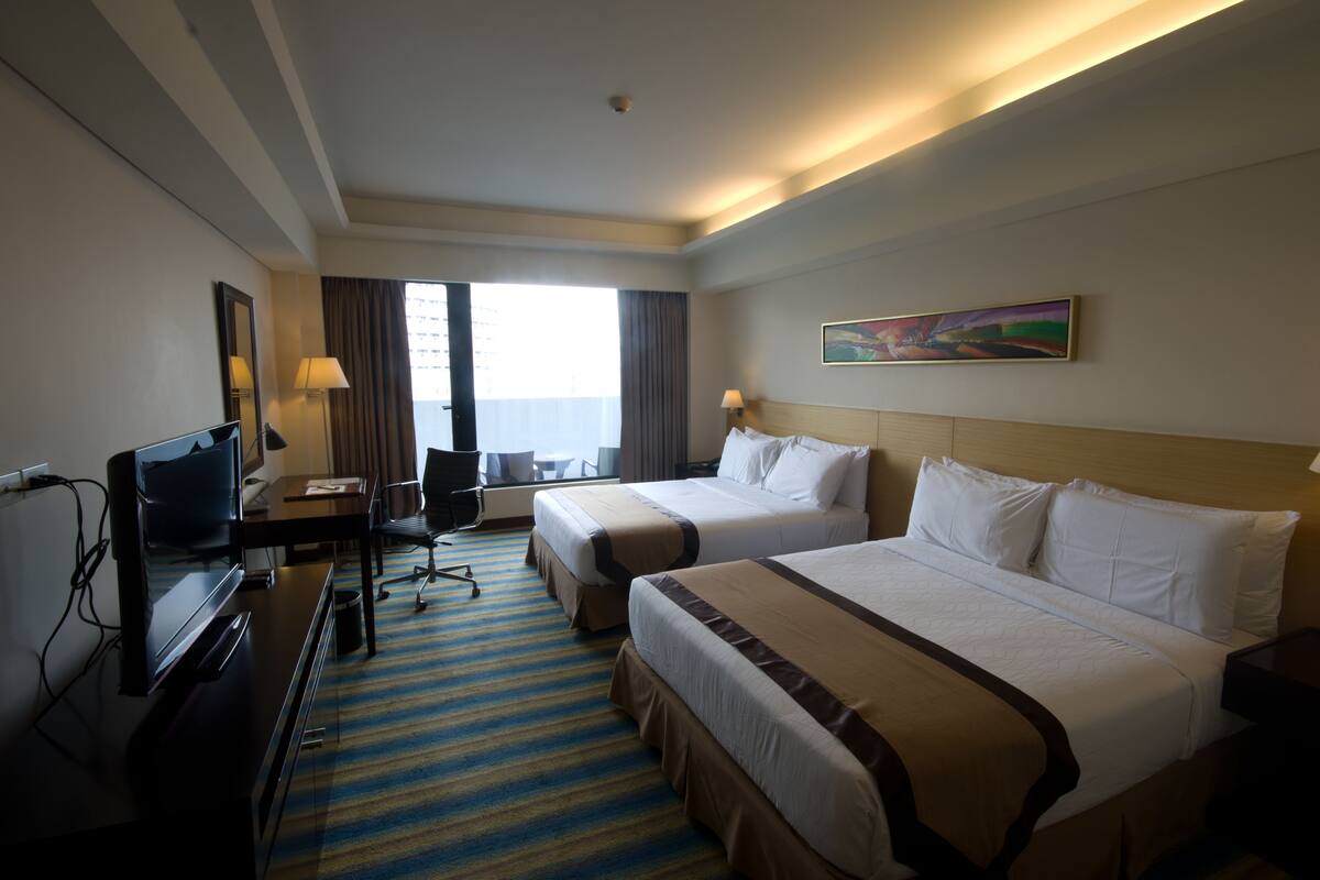 A hotel room with two beds, a desk with a TV, a chair, and a window with curtains.