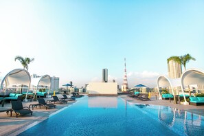 A rooftop pool with lounge chairs and umbrellas, surrounded by modern buildings and a tall tower. - Luxent Hotel (Quezon City)