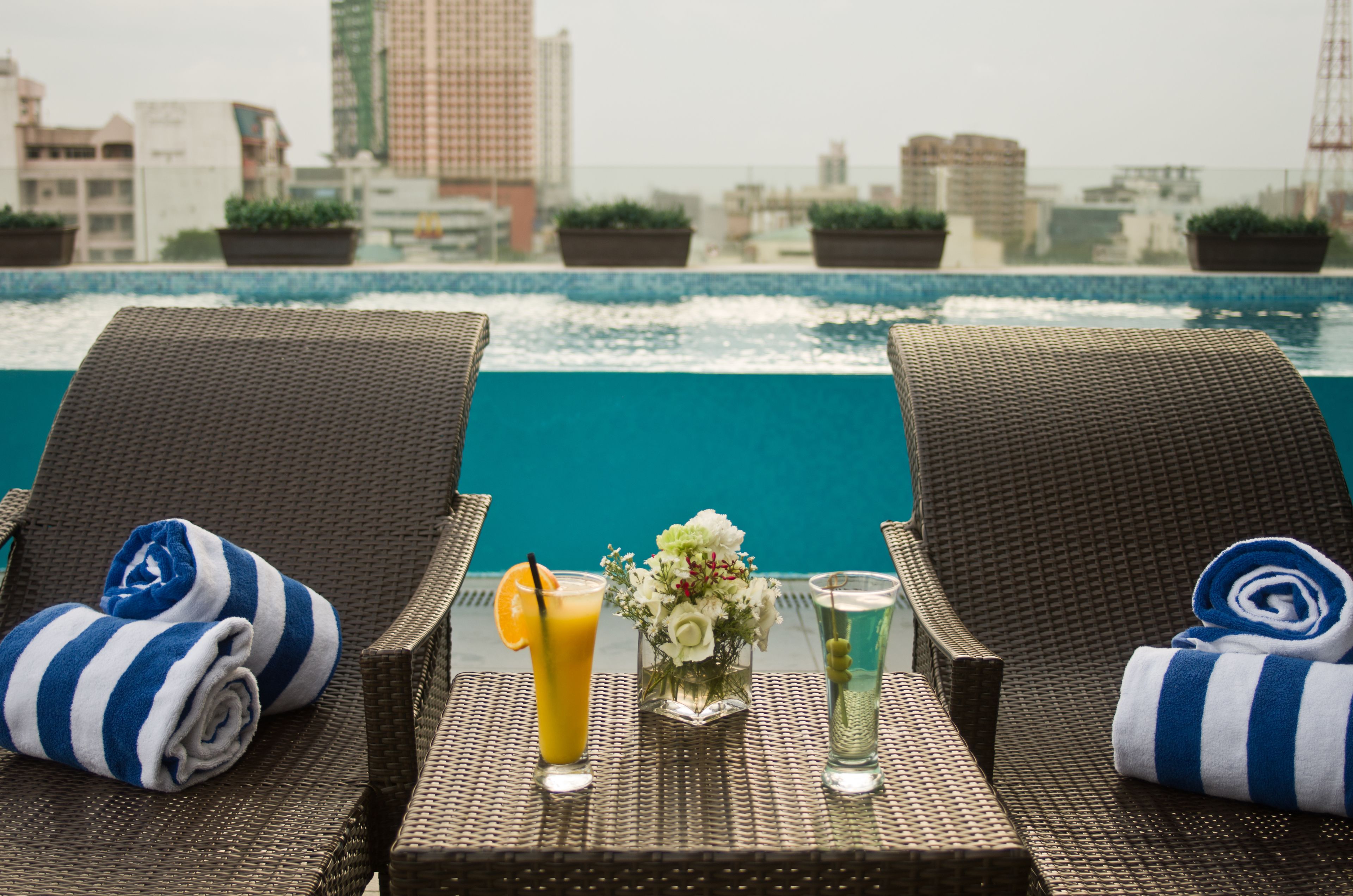 Two wicker lounge chairs with blue and white striped towels, a glass of orange juice, a glass of water, and a vase with white flowers.