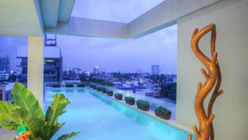 A rooftop pool area with a view of the city skyline, potted plants, and a sculptural piece.