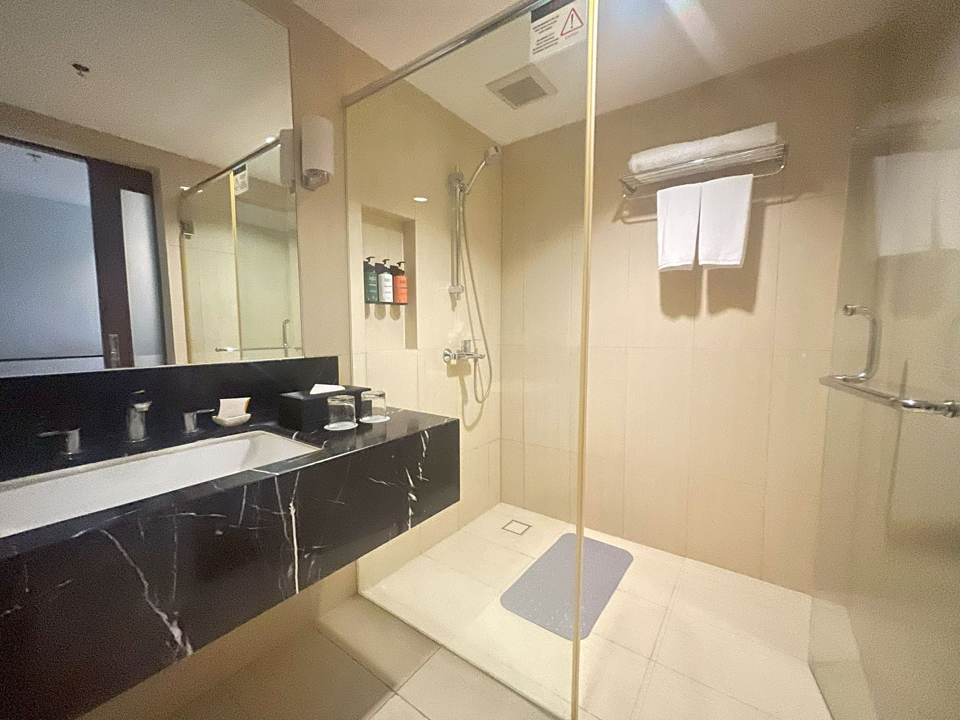 A modern bathroom with a black marble sink, a glass shower enclosure, and a white towel hanging on the wall.