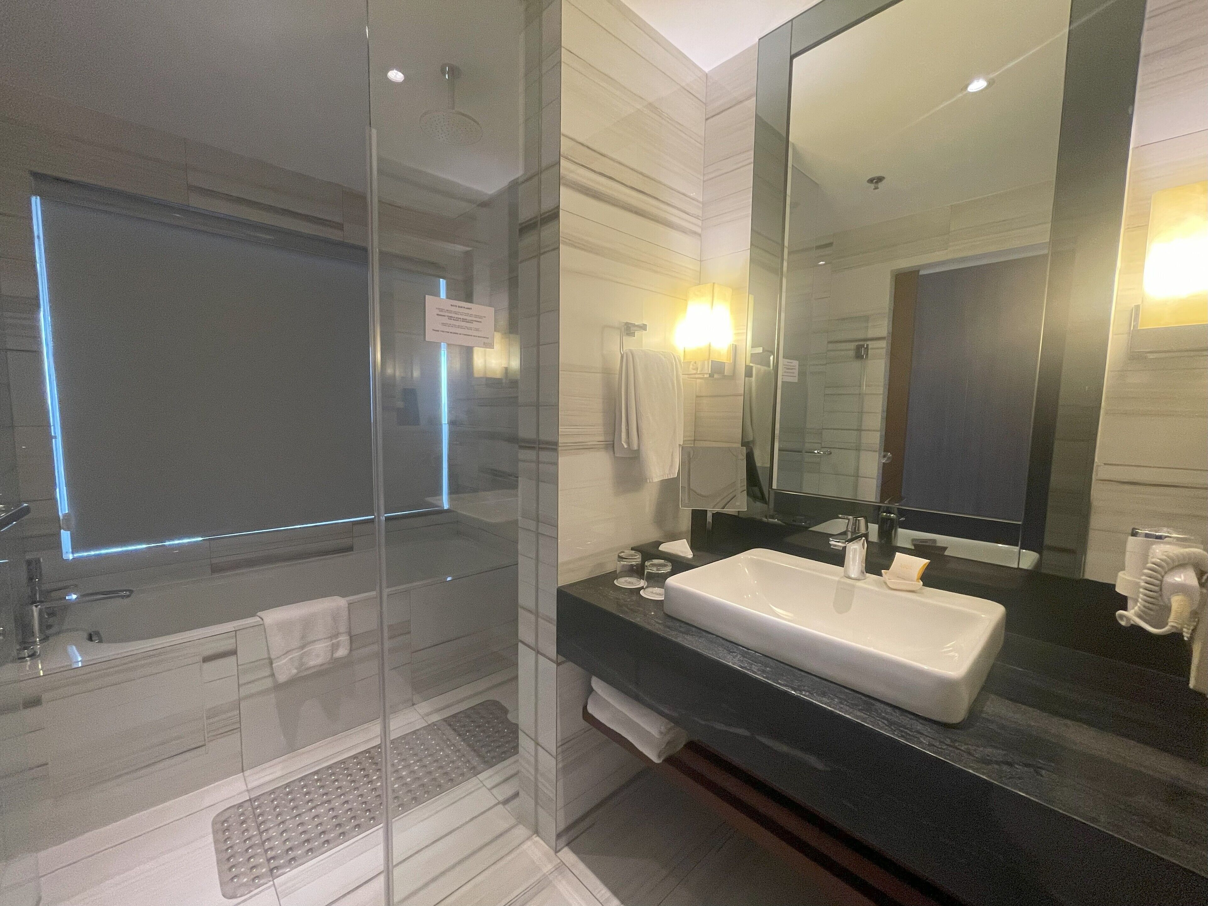 Un baño moderno con ducha envuelta en vidrio, un espejo grande y un lavabo blanco.