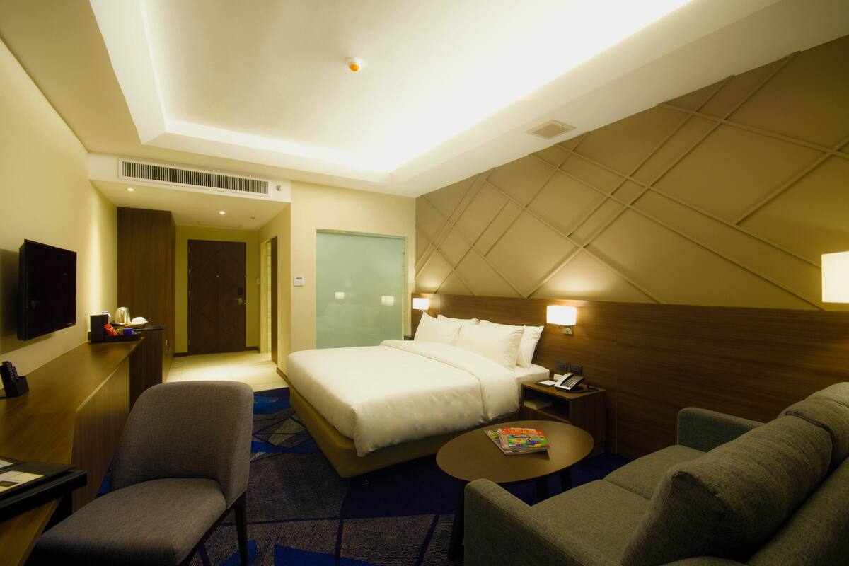 A hotel room with a bed, a desk with a chair, a small table, and a TV.