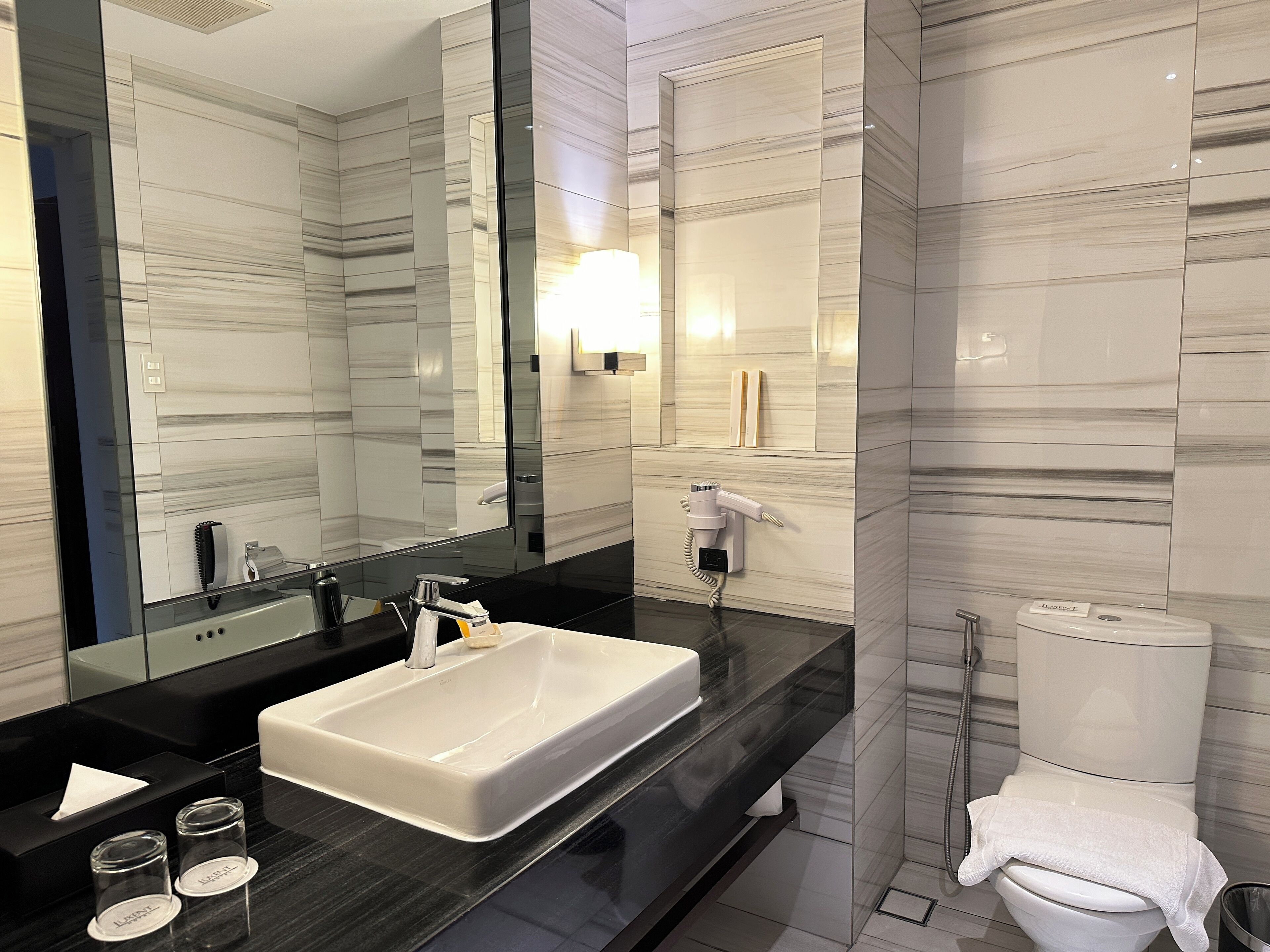 A modern bathroom with a large mirror, a white sink, a black countertop, and a toilet.