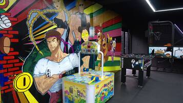 Una habitació decorada amb llum, amb taula de futbolí, taula de billar i un mural amb personatges de dibuixos animats.