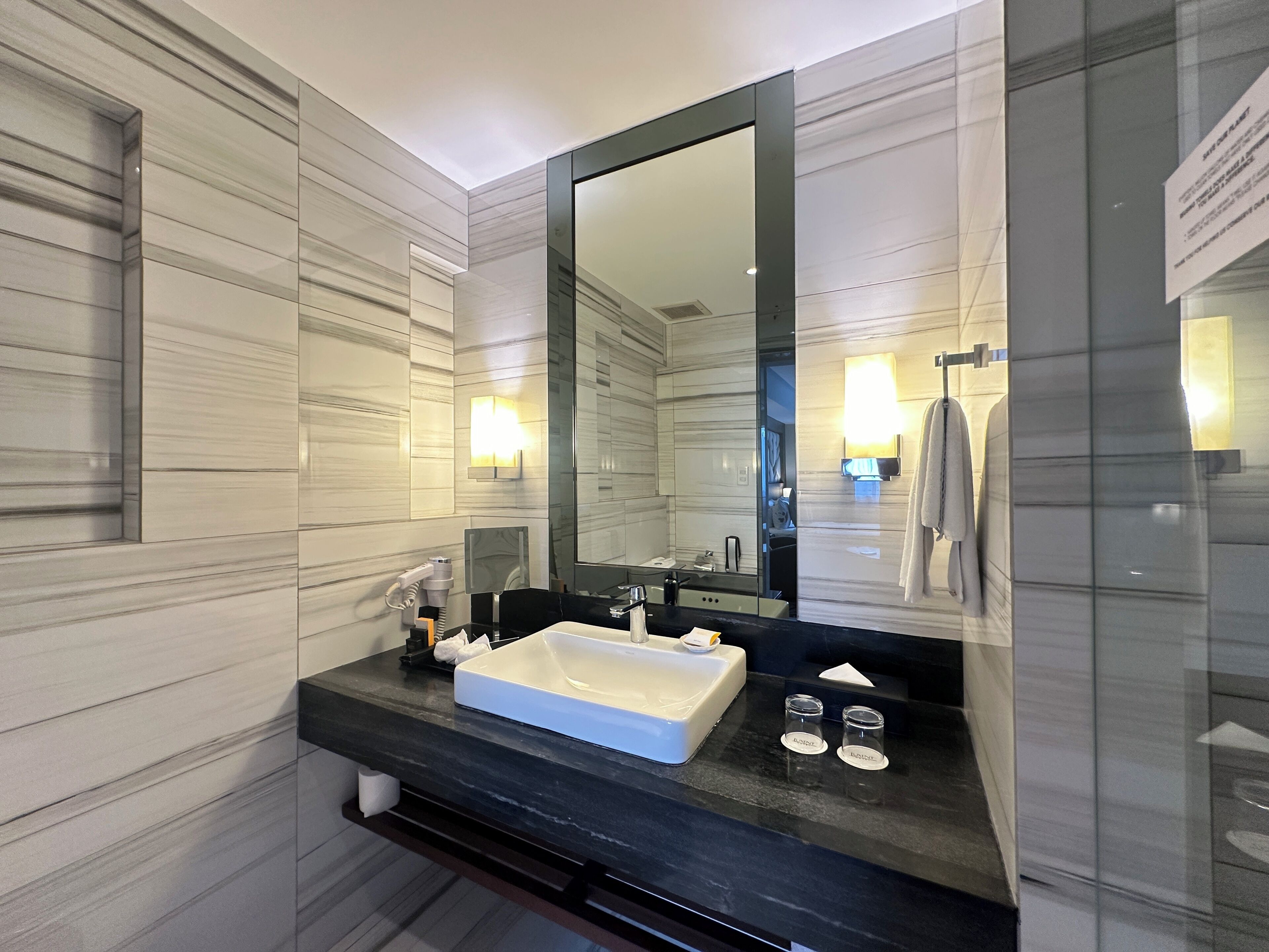 A modern bathroom with a large mirror, a black countertop, a white sink, and a towel rack.