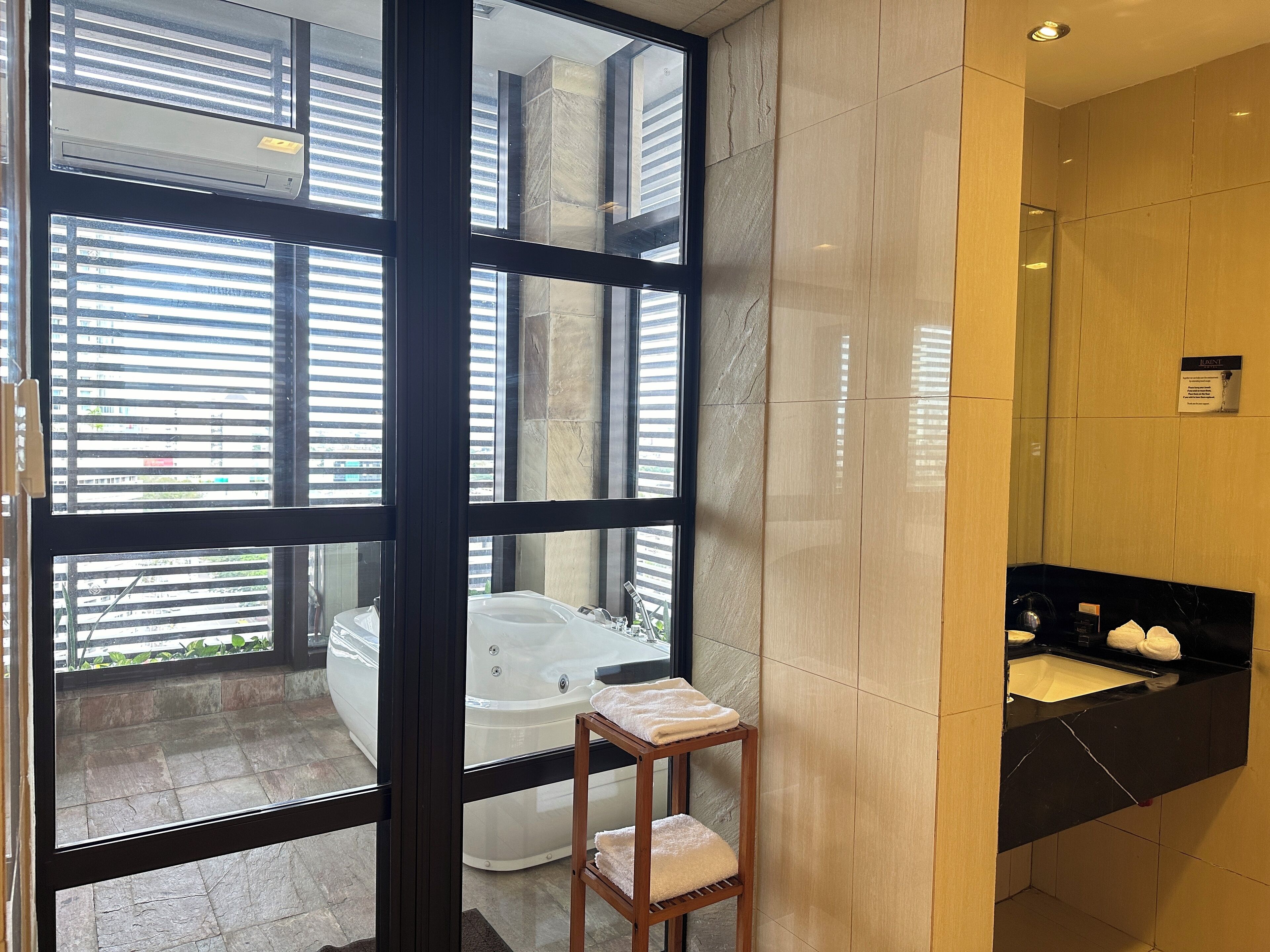 A modern bathroom with a glass-enclosed window, a bathtub, a vanity with a sink, and a towel rack.