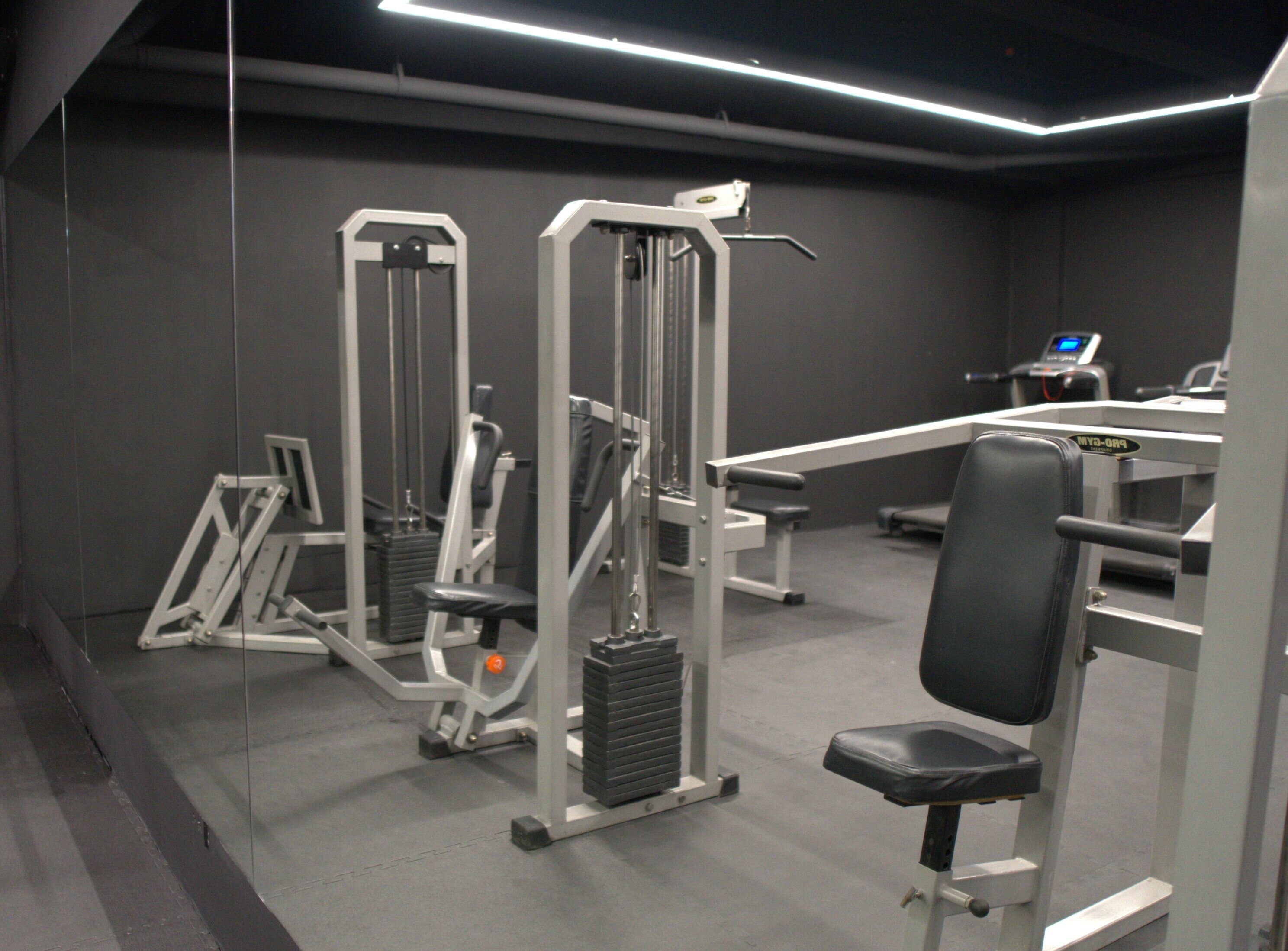 A gym with various exercise machines, a bench, and a digital display.