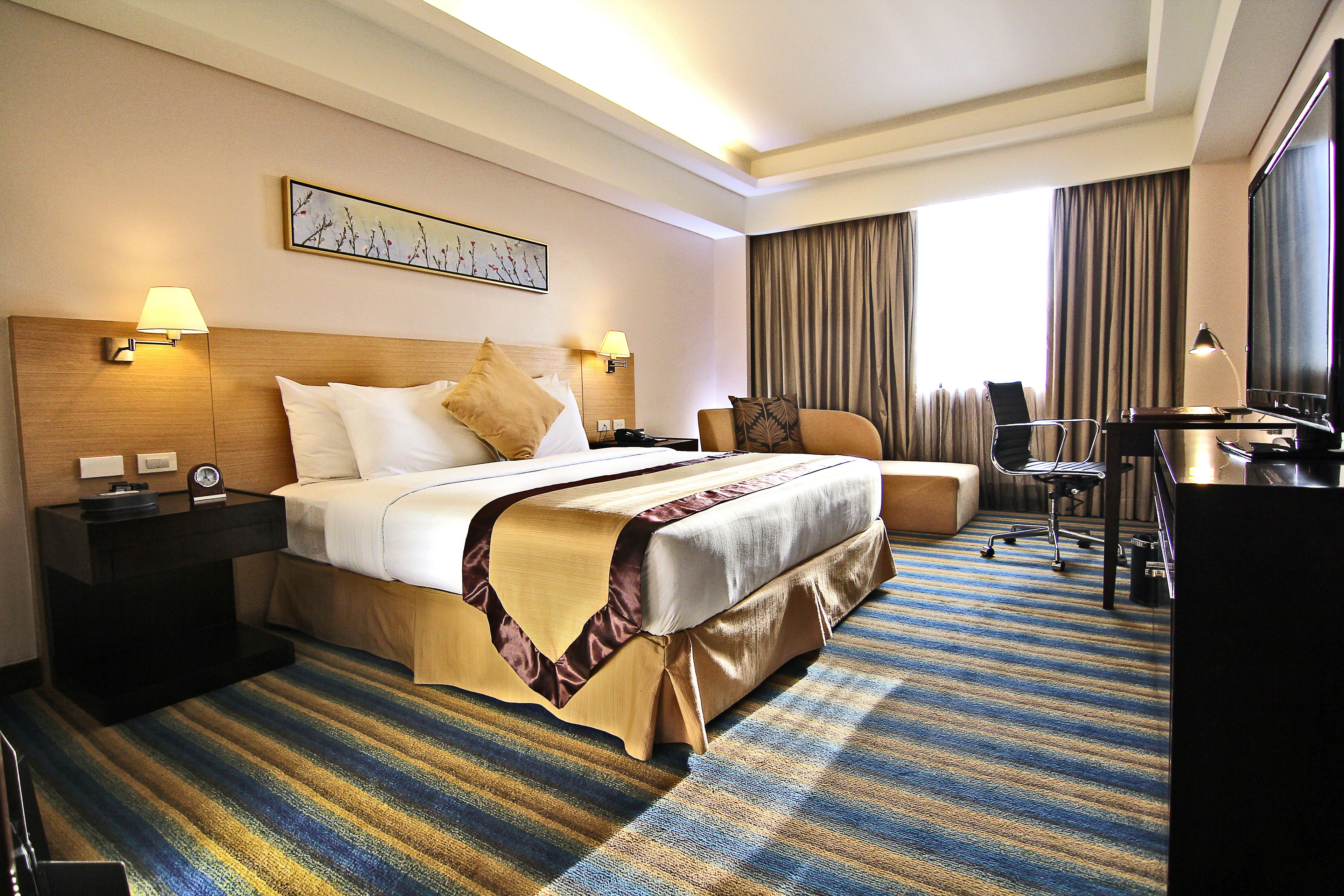 A hotel room with a large bed, a desk, a chair, and a television.