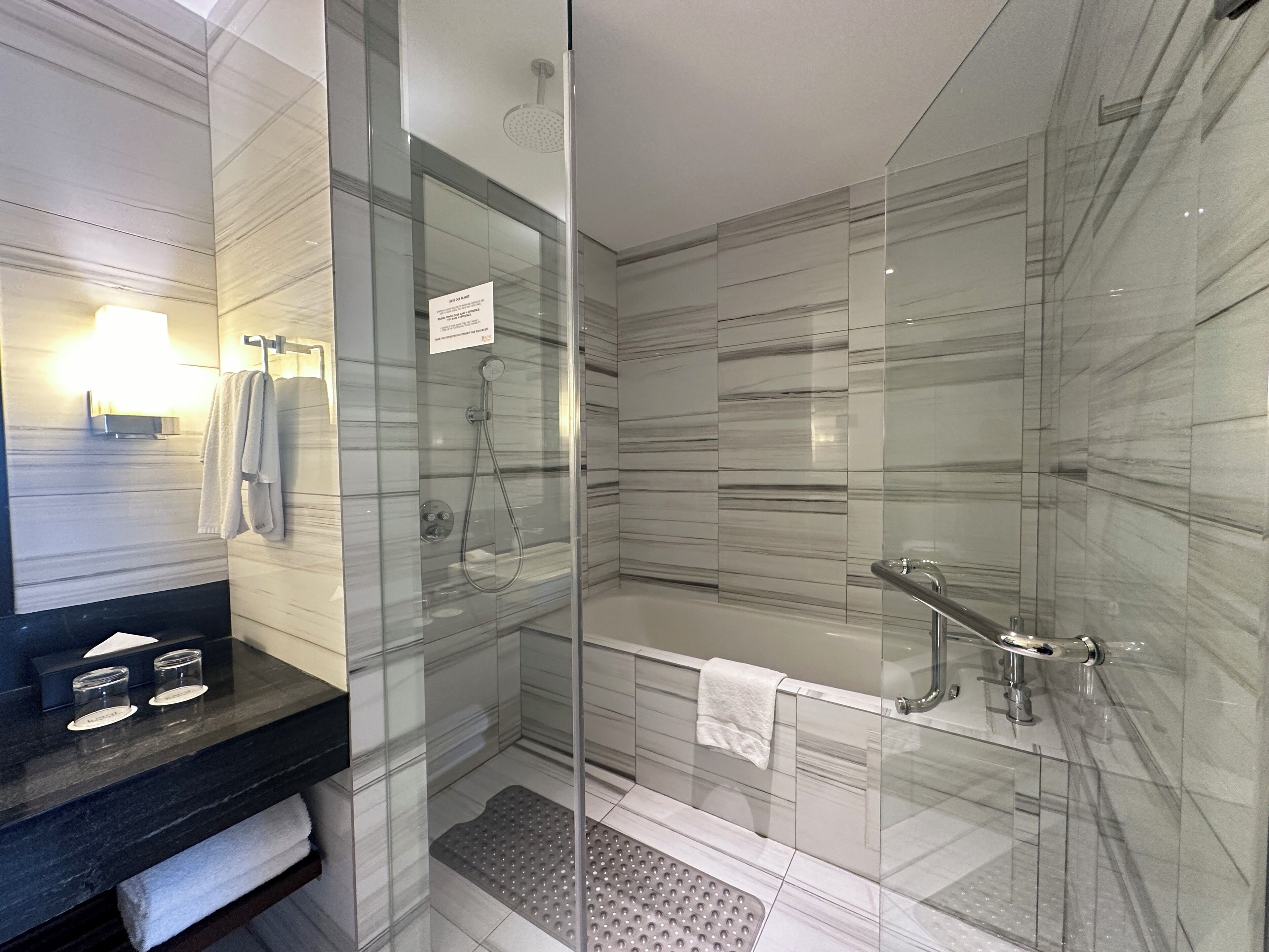 A modern bathroom with a glass-enclosed shower, a separate bathtub, and a vanity with a towel rack.